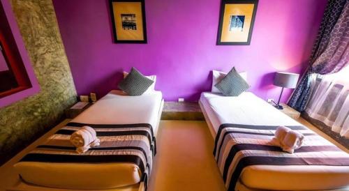two beds in a room with purple walls at The B Ranong Trend Hotel in Ranong
