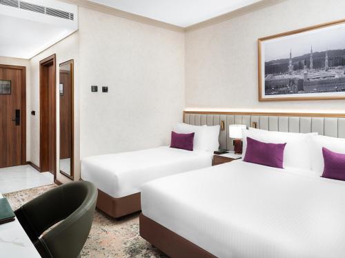 a hotel room with two beds and a chair at Elaf Taiba Hotel in Al Madinah