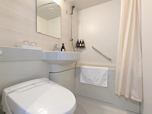 a white bathroom with a toilet and a sink at Odysis Sapporo Odori Koen Hotel in Sapporo