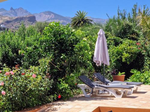 ein Sonnenschirm und zwei Liegestühle mit Bergen im Hintergrund in der Unterkunft Casa con piscina privada y vistas in Santa Brígida