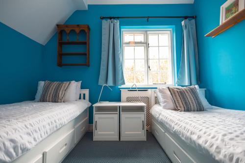 a blue bedroom with two beds and a window at Lavender Cottage in Burley