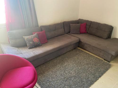 a brown couch in a living room with a pink chair at Bloome appartement, Riadh Andalous , Ariana ville in Burj at Turkī