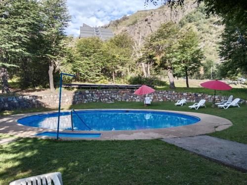 a swimming pool with two umbrellas and two white chairs at Nevados de chillan , edificio los coigues in Nevados de Chillan