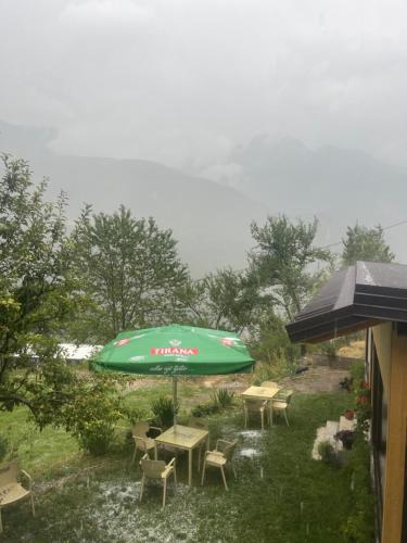 a green umbrella and tables and chairs in a yard at Guesthouse Te Tata in Theth
