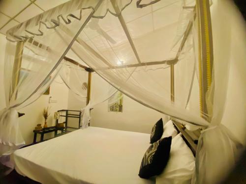 a bedroom with a canopy bed with white sheets and pillows at Zensigiri Ayurveda Wellness Homestay in Sigiriya