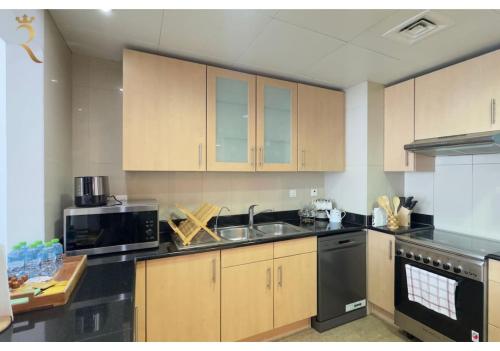 a kitchen with wooden cabinets and a sink and a microwave at Al Reem 2BR - Stylish Family Retreat in Abu Dhabi