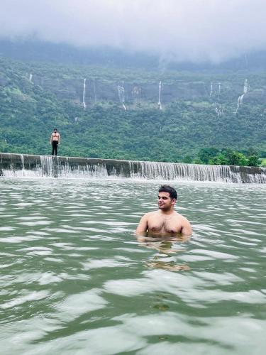 a man in the water in front of a waterfall at Katha Villa 63 - Luxury Holiday Home in Karjat