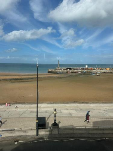 a person walking on a sidewalk near a beach at Seaside Apartment, on the doorstep of the Beach! in Margate