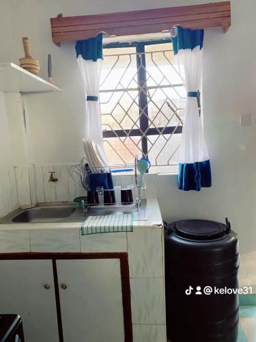 a kitchen with a window with blue and white curtains at Chief engineer apartment in Mwingi