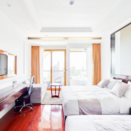 a white bedroom with two beds and a desk and a chair at GoldOne Hotel & Suites in Seogwipo