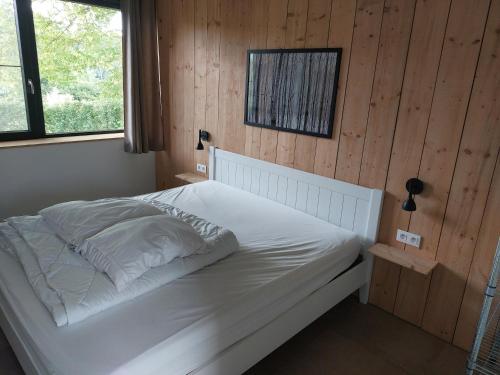 a white bed in a room with a wooden wall at Champs Erezée , genieten in elk seizoen in Érezée