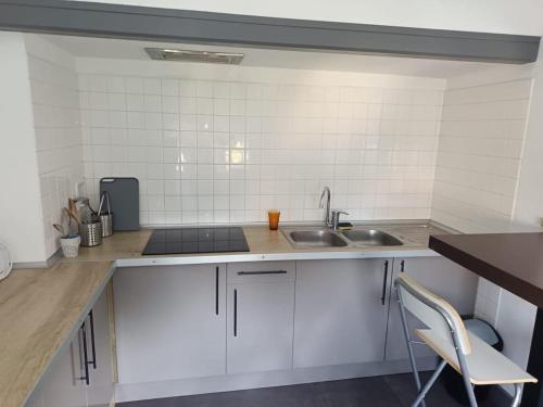 a kitchen with white cabinets and a sink and a chair at Le Nid - 2 Bedrooms - Myra Conciergerie in Gan