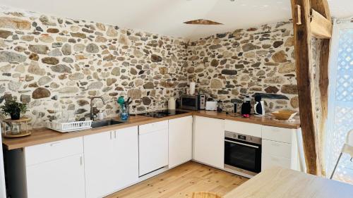 a kitchen with white cabinets and a stone wall at Le Refuge du Cagire in Aspet