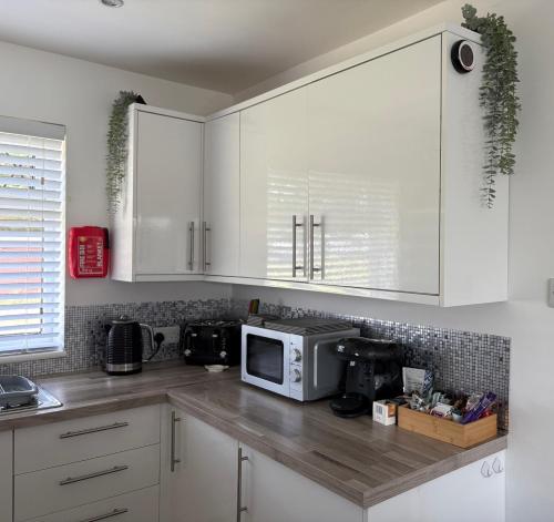 a kitchen with white cabinets and a microwave at 46 Gower Holiday Village in Swansea