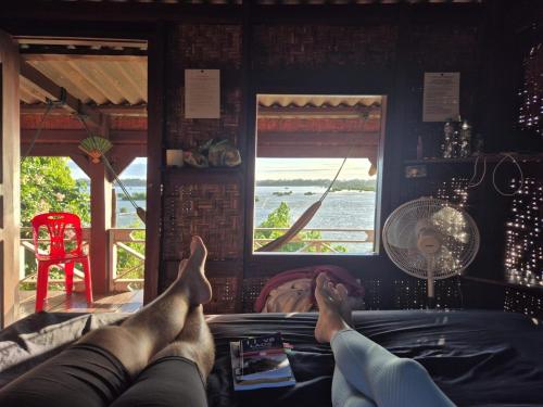 a person laying on a bed looking out the window at Don Som Riverside Guesthouse in Don Som