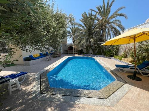 a swimming pool with an umbrella and two chairs and an umbrella at La Villa Bleue Djerba Houmt Souk in Houmt Souk