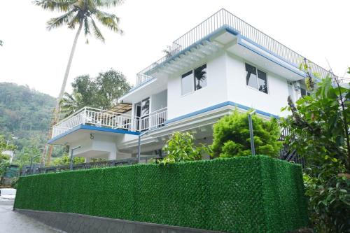 a white house with a green hedge in front of it at Cardamom Crush Premium Villa in Munnar
