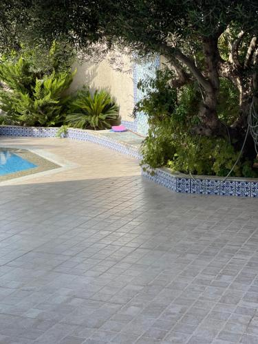 a tile walkway next to a swimming pool with a tree at La Villa Bleue Djerba Houmt Souk in Houmt Souk