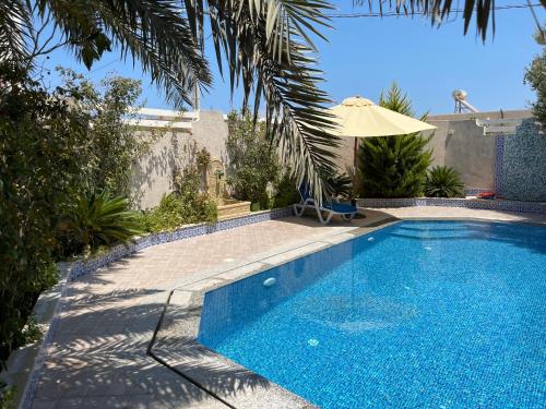 a swimming pool with an umbrella next to a house at La Villa Bleue Djerba Houmt Souk in Houmt Souk