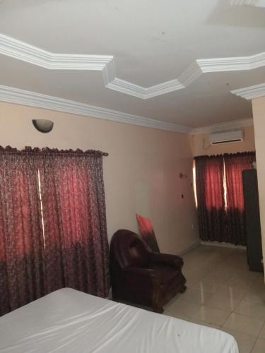 a room with a chair and a bed and curtains at AFRICAN PRINCESS HOTEL, New Haven in Enugu