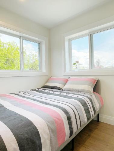 a bed in a white room with two windows at A Beautiful, cozy second floor room for staying in Vancouver
