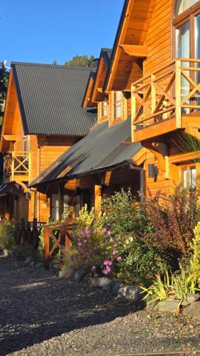 a wooden house with a balcony and some flowers at Apart Hotel Agua Escondida in San Martín de los Andes