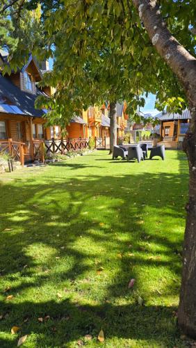a green yard with picnic tables and a tree at Apart Hotel Agua Escondida in San Martín de los Andes