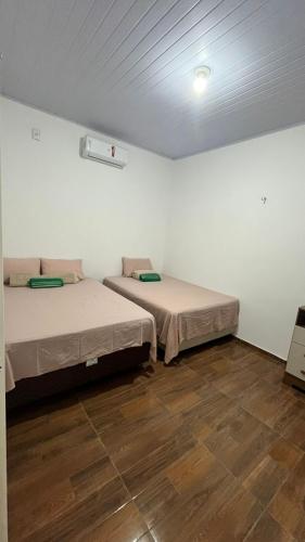 two beds in a room with white walls and wooden floors at Casa com dois quartos e piscina in Barreirinhas