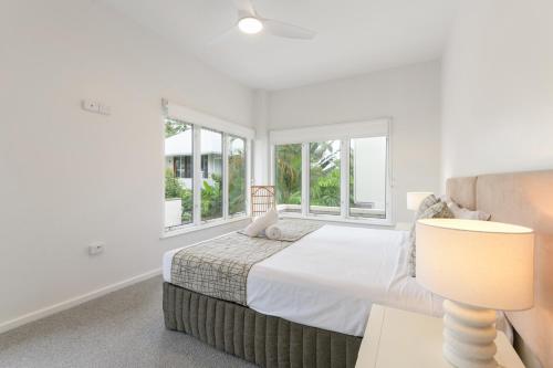 a bedroom with a bed with a lamp and windows at Balboa Apartments in Port Douglas
