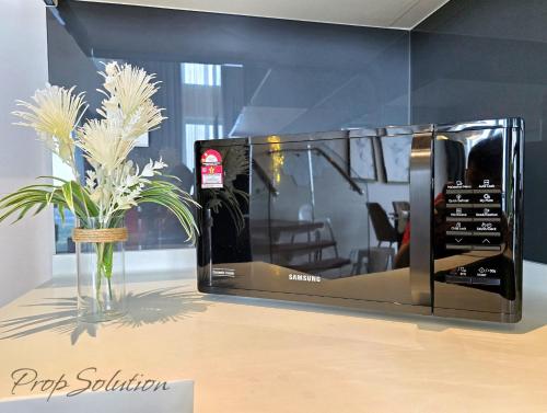 a black microwave sitting on a table with a vase of flowers at Spacious Cozy Elysia Suite Johor Bahru Legoland in Iskandar Puteri
