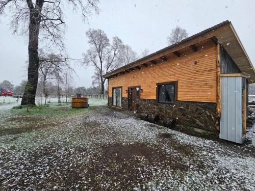 une cabane en rondins avec de la neige au sol à côté d'un arbre dans l'établissement Tierra de Volcanes, à Curacautín