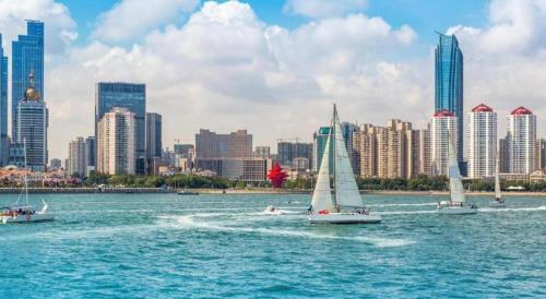 three sailboats in the water in front of a city at Jinjiang Inn Qingdao Wuxi Square Nanjing Road Metro Station in Qingdao