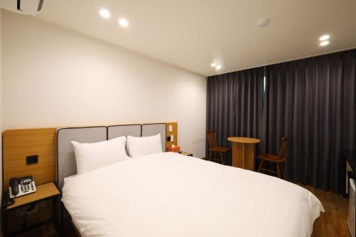 a bedroom with a white bed and a table and chairs at JB Plus Hotel in Busan