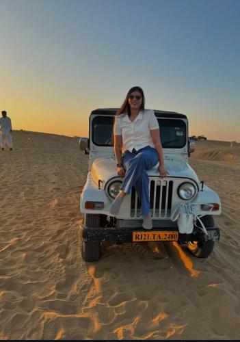 a woman sitting on the bonnet of a jeep in the desert at The Desert Resort Jaisalmer in Jaisalmer