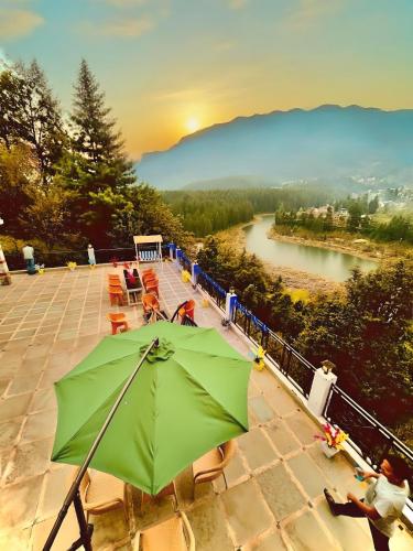 a green umbrella sitting on a patio next to a river at Hotel Hollywood Manali - Scenic River & Mountain View With Premium Rooms Near Mall Road in Manāli