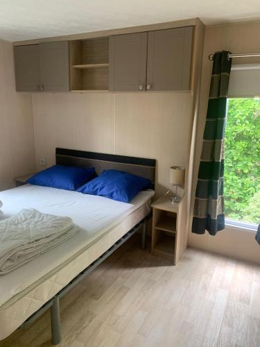 a bedroom with a bed with blue pillows and a window at Chalets van Minicamping De Braamhof in Koudekerke