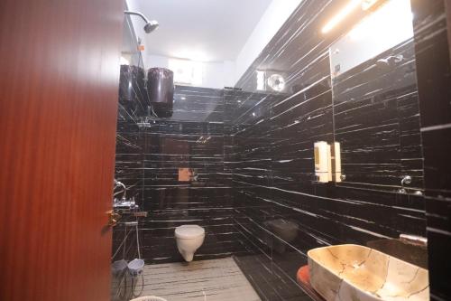 a black tiled bathroom with a tub and a toilet at Hotel Maharani Grand Patna in Patna