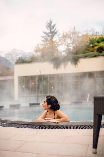 a woman is sitting in a swimming pool at Hotel Mignon Meran Park & Spa in Merano