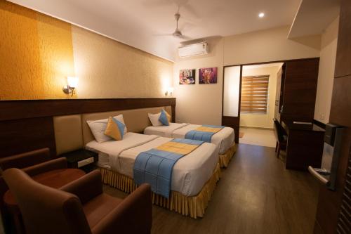 a hotel room with two beds and a chair at Hotel High Point in Tiruchchirāppalli