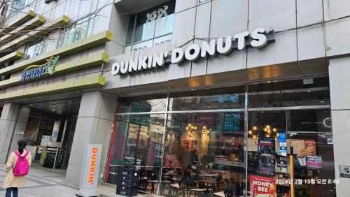 a woman walking in front of a dunkin donuts store at Hongdae Home Sweet Home in Seoul