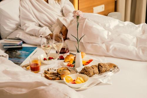 a woman sitting in bed with a tray of food and drinks at Hotel Mignon Meran Park & Spa in Merano