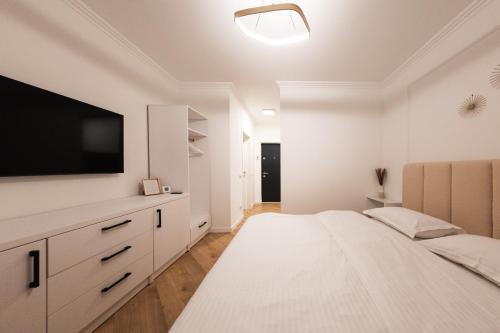 a white bedroom with a large bed and a flat screen tv at Nest Inn Velvet Apartment in Baia Mare