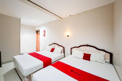 two beds in a room with white and red sheets at RedDoorz Hotel Tejomoyo Near Bukit Sekipan Tawangmangu in Tawangmangu