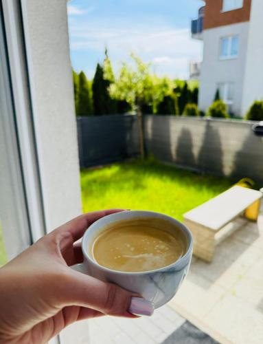 a person holding a cup of coffee on a balcony at LUX Apartament in Suwałki
