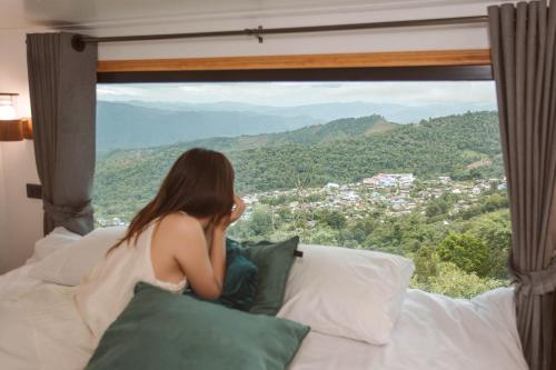 a woman sitting on a bed looking out of a window at Sinsup villa Doichang 2 in Ban Huai Khai