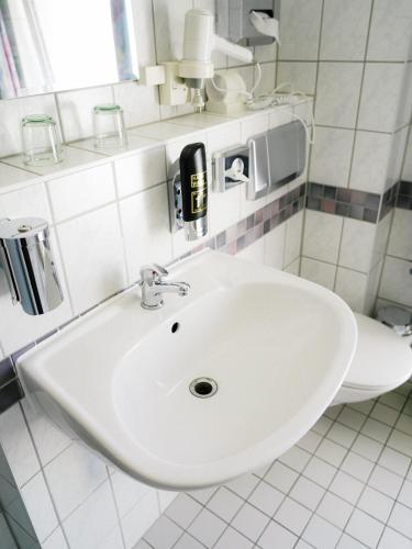 a white sink in a white tiled bathroom at Apart Hotel Leipzig Taucha in Taucha