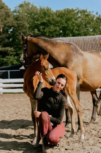 a woman kneeling next to a baby horse next to a horse at Apartamenty Pod Dębami Stadnina Koni SPA Jezioro i Morze Sarbsk in Sarbsk