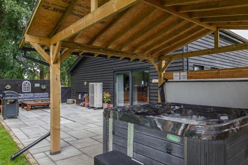 a patio with a grill and a wooden pergola at Owl Barn - Norfolk in Saham Toney