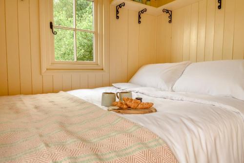 a bed with a tray of croissants and a plate of bread at The Orchard Hut in Burnham Market