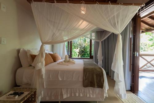 a bedroom with a white bed with a canopy at Pousada Cajueiro Trancoso in Trancoso